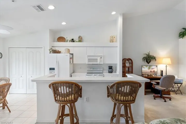 Kitchen featuring light countertops, white appliances, a breakfast bar, and visible vents