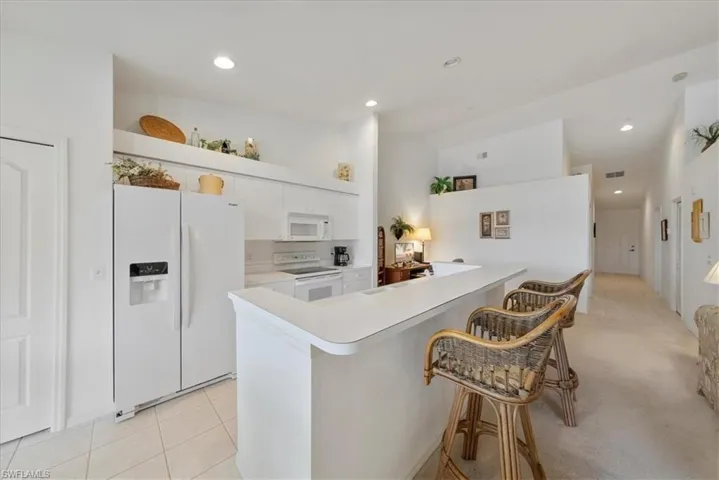 Kitchen with white appliances, a kitchen breakfast bar, light countertops, white cabinetry, and light tile patterned flooring
