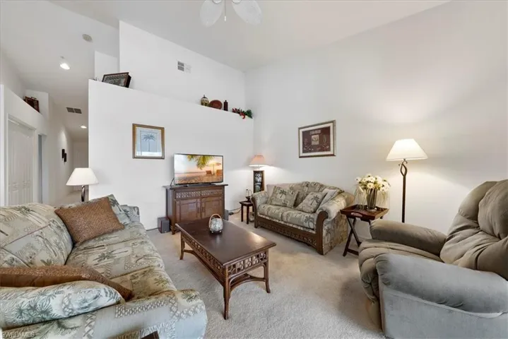 Living area featuring a high ceiling, visible vents, and light colored carpet