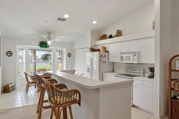 Kitchen with a breakfast bar, white appliances, white cabinetry, and light tile patterned floors
