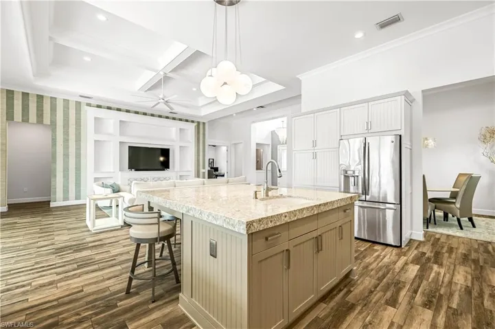 Kitchen featuring hanging light fixtures, stainless steel refrigerator with ice dispenser, open floor plan, a breakfast bar area, and coffered ceiling