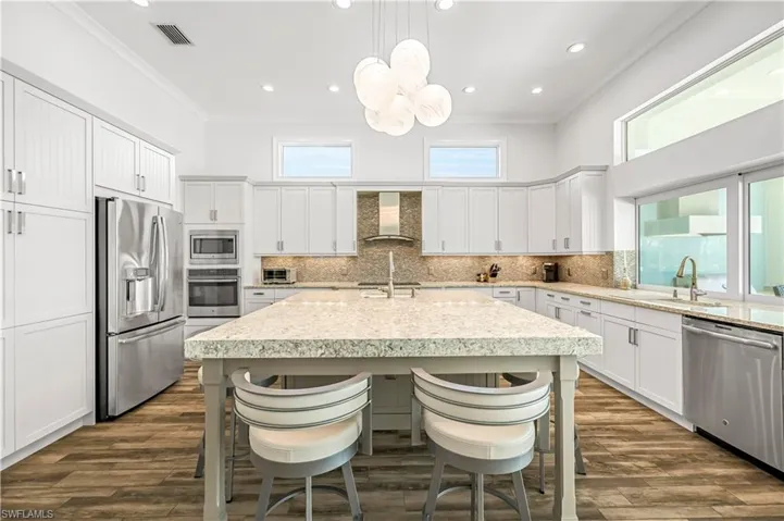 Kitchen with stainless steel appliances, backsplash, crown molding, white cabinets, and pendant lighting