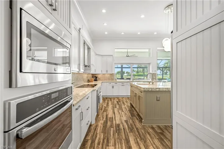 Kitchen with stainless steel appliances, pendant lighting, dark wood finished floors, light stone countertops, and decorative backsplash