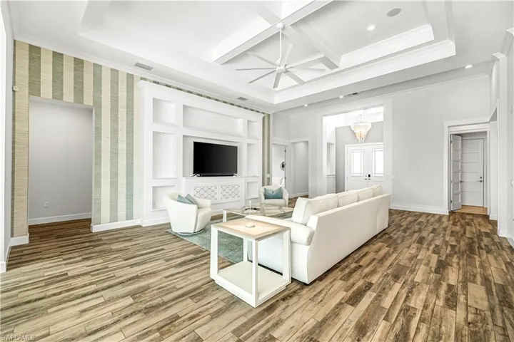 Living area with wood finished floors, coffered ceiling, ceiling fan, beamed ceiling, and crown molding
