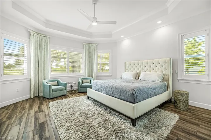 Bedroom with a tray ceiling, crown molding, ceiling fan, dark wood-style flooring, and recessed lighting