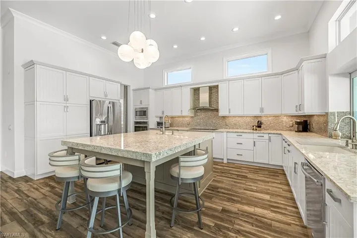 Kitchen featuring crown molding, pendant lighting, stainless steel appliances, light stone countertops, and tasteful backsplash