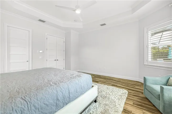 Bedroom featuring a raised ceiling, wood finished floors, ornamental molding, and ceiling fan