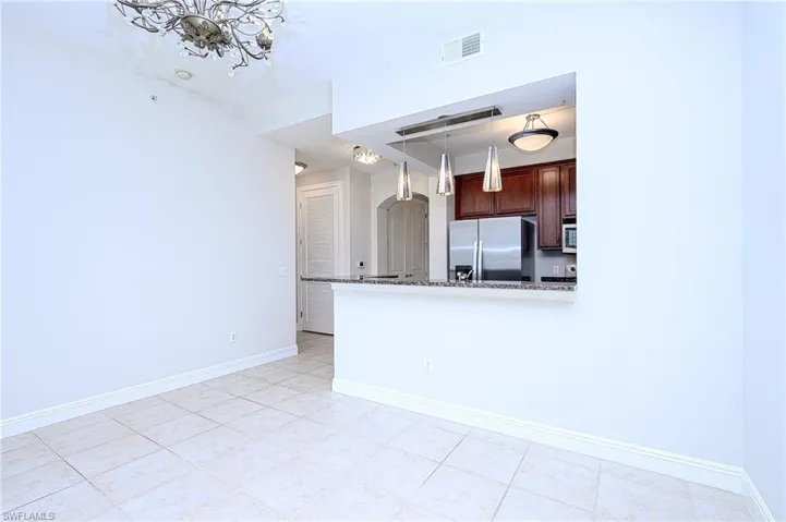 Kitchen with pendant lighting, stainless steel fridge with ice dispenser, kitchen peninsula, light tile patterned floors, and stone counters