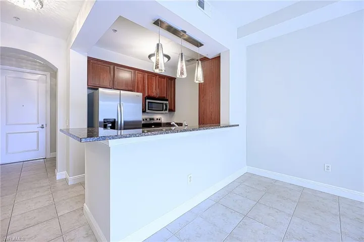 Kitchen with appliances with stainless steel finishes, dark stone countertops, hanging light fixtures, kitchen peninsula, and light tile patterned flooring