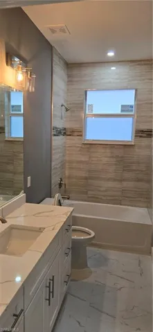 Bathroom featuring shower / tub combination, marble look tiles, toilet, healthy amount of natural light, and recessed lighting