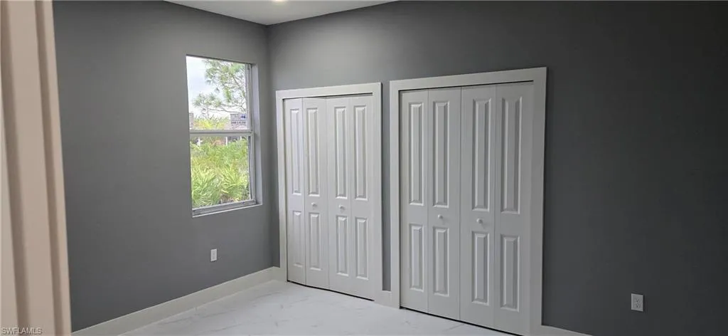 Unfurnished bedroom with multiple closets, multiple windows, light marble finish floors, and baseboards