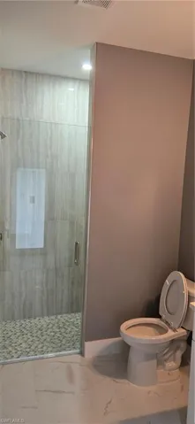 Full bathroom featuring marble finish flooring, toilet, and a shower stall