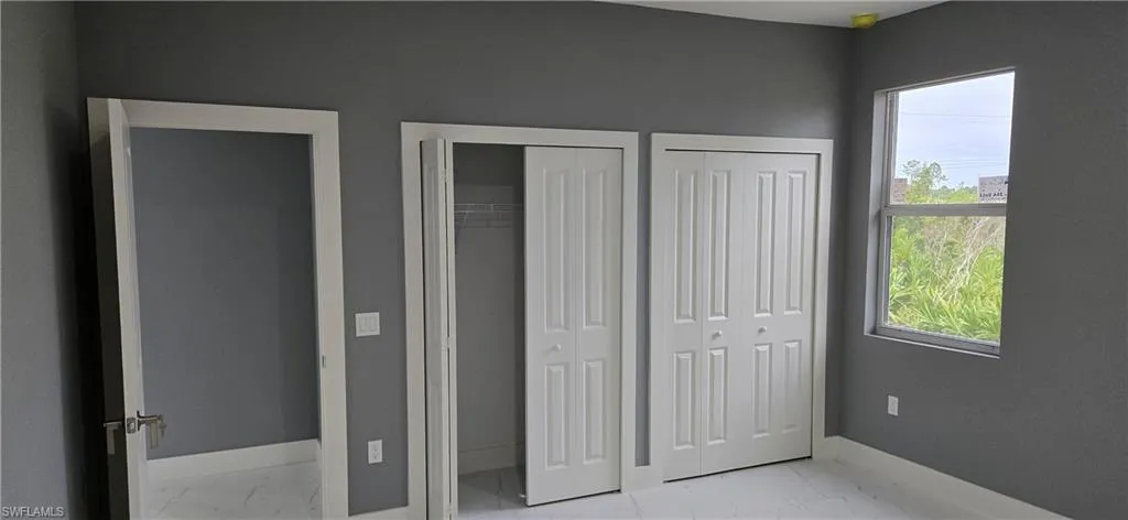 Unfurnished bedroom featuring light marble finish flooring, baseboards, and two closets