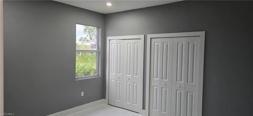 Unfurnished bedroom featuring multiple closets, multiple windows, light marble finish flooring, baseboards, and recessed lighting