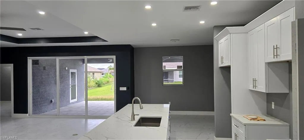 Kitchen with a sink, baseboards, light stone countertops, white cabinetry, and recessed lighting