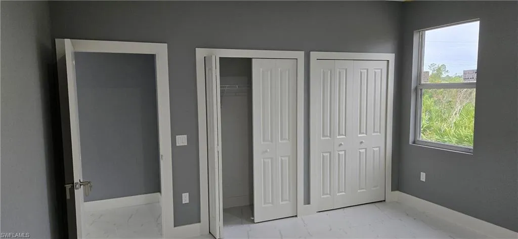 Unfurnished bedroom featuring marble finish floors, baseboards, and two closets