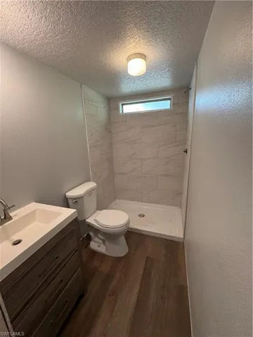 Modern bathroom featuring a wood-finish vanity with an integrated sink, a white toilet, and a walk-in shower with tiled walls