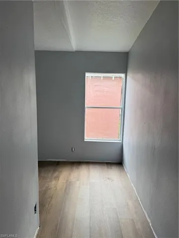 Room featuring a single window, light gray painted walls, and wood-finish flooring