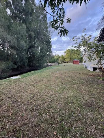 Expansive grassy area featuring mature trees along the perimeter and a red storage shed