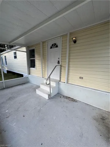 Covered porch entry featuring a decorative paneled door with an arched window insert, exterior wall light fixture, and a three-step entry with a metal handrail