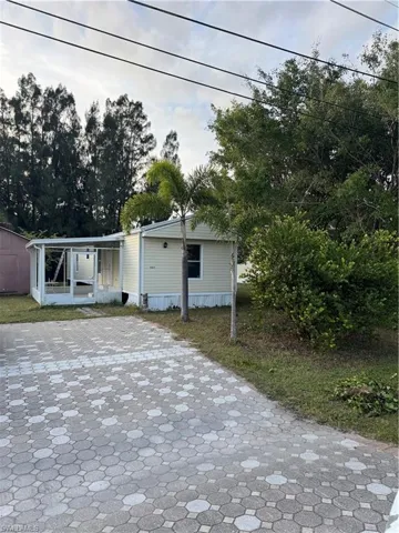 Residential structure with light-toned siding, featuring a covered patio enclosure and a patterned paver driveway