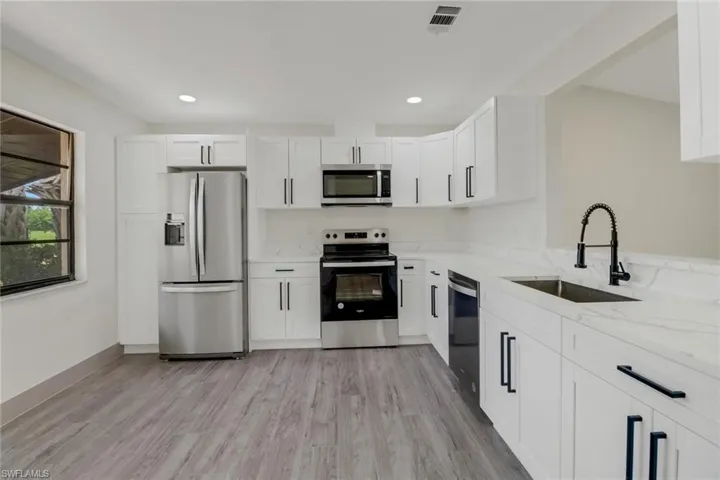 Kitchen with sink, light stone countertops, light hardwood / wood-style flooring, and stainless steel appliances