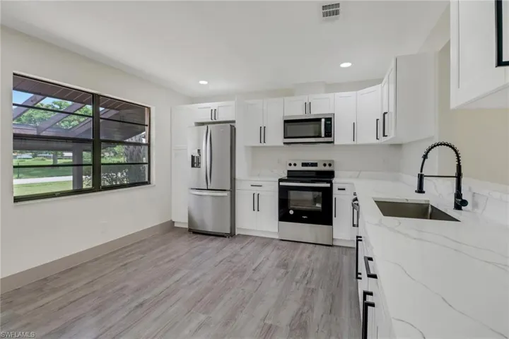 Kitchen with light hardwood / wood-style flooring, stainless steel appliances, sink, light stone counters, and white cabinetry