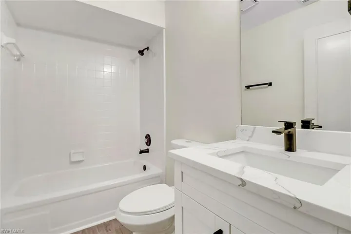 Full bathroom with hardwood / wood-style floors, toilet, vanity, and tiled shower / bath