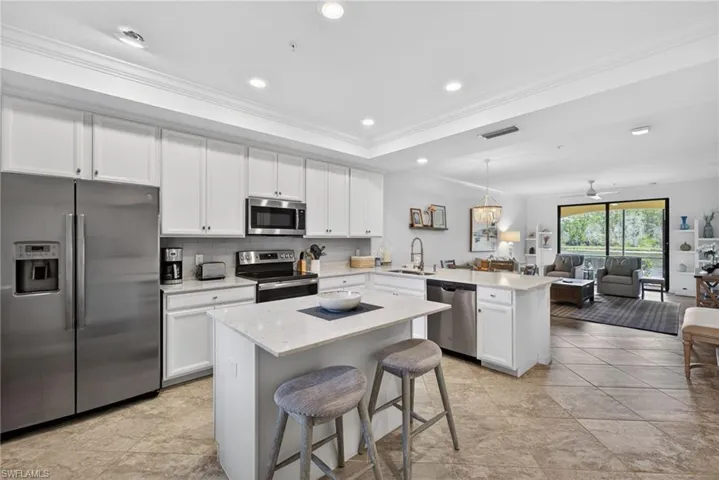 Open-concept kitchen featuring white cabinetry, stainless steel appliances, and a central island with a solid surface countertop