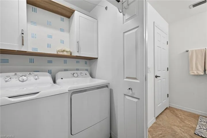 Laundry area featuring a side-by-side washer and dryer, wood-finish shelving, and white upper cabinetry with brushed nickel hardware