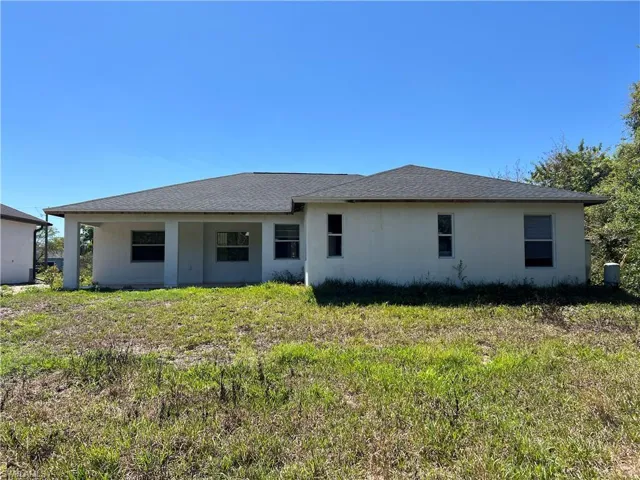 Rear view of property featuring stucco siding, a lawn, and roof with shingles