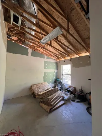 Bedroom with concrete flooring, a garage, and vaulted ceiling