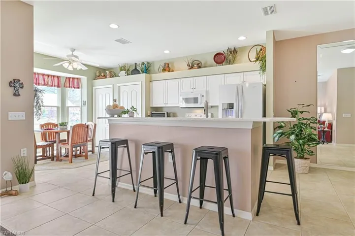 Kitchen featuring light tile patterned flooring, a breakfast bar, white appliances, and white cabinets
