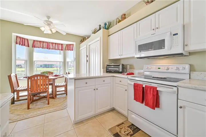 Kitchen with white appliances, kitchen peninsula, light tile patterned flooring, white cabinetry, and ceiling fan
