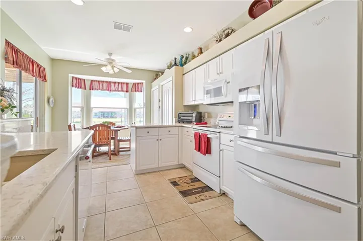 Kitchen featuring white cabinets, light tile patterned flooring, white appliances, and ceiling fan