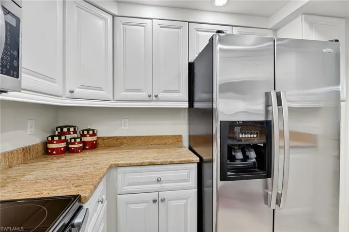 Kitchen featuring stainless steel refrigerator with ice dispenser, white cabinets, black electric range, light countertops, and recessed lighting