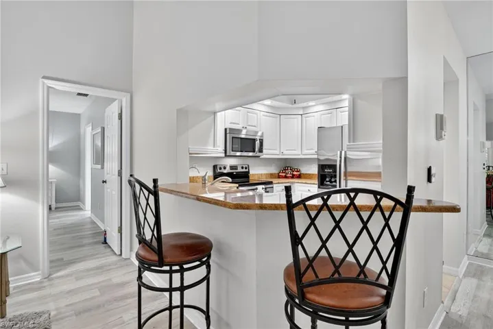 Kitchen with stainless steel appliances, a breakfast bar area, white cabinets, light wood-style floors, and a peninsula