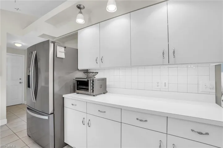 Kitchen with light tile patterned flooring, stainless steel fridge, white cabinets, and backsplash