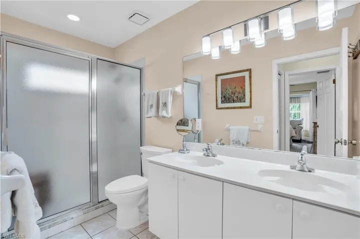 Bathroom featuring a shower with door, double vanity, toilet, and tile patterned floors