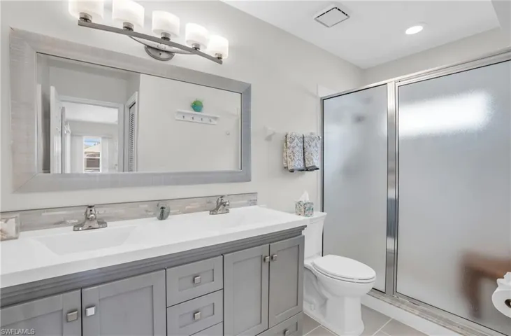 Bathroom featuring an enclosed shower, tile patterned flooring, toilet, and dual bowl vanity