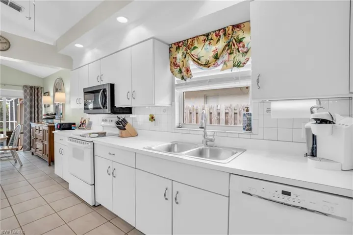 Kitchen featuring light tile patterned flooring, white cabinetry, tasteful backsplash, white appliances, and sink