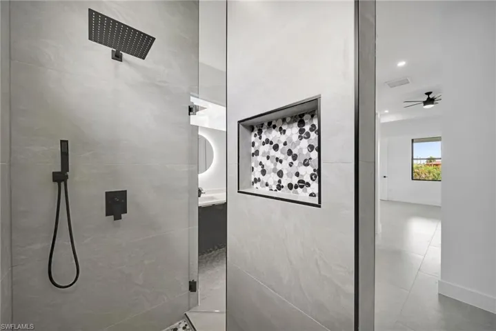 Bathroom with tiled shower, tile patterned flooring, vanity, and ceiling fan