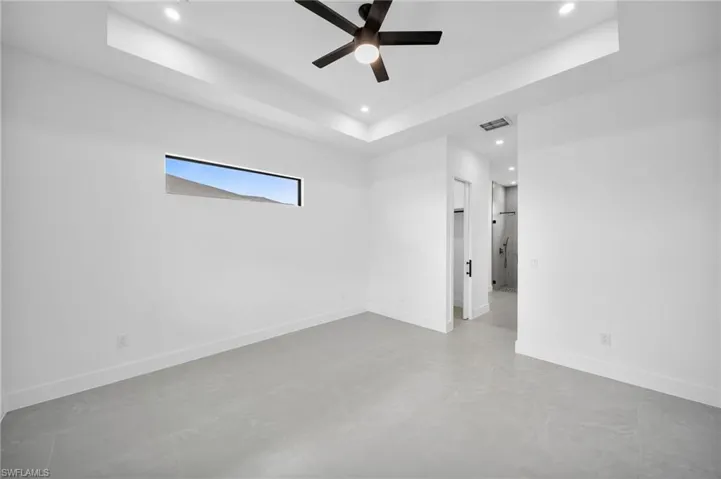 Tiled empty room featuring ceiling fan and a raised ceiling
