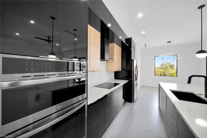 Kitchen with black electric cooktop, hanging light fixtures, sink, double oven, and light tile patterned floors