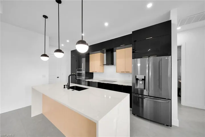 Kitchen with wall chimney range hood, an island with sink, hanging light fixtures, appliances with stainless steel finishes, and sink