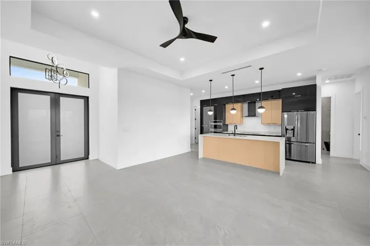 Kitchen with hanging light fixtures, a tray ceiling, stainless steel appliances, and a center island with sink