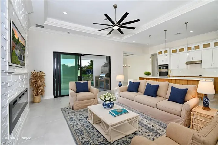 Living room with a fireplace, a tray ceiling, light tile patterned floors, ceiling fan, and ornamental molding