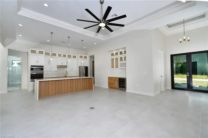 Kitchen with glass insert cabinets, pendant lighting, a tray ceiling, a large island, and ornamental molding