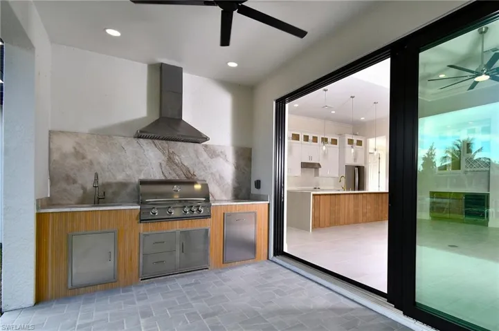 Kitchen featuring ceiling fan, glass insert cabinets, wall chimney exhaust hood, white cabinetry, and fridge