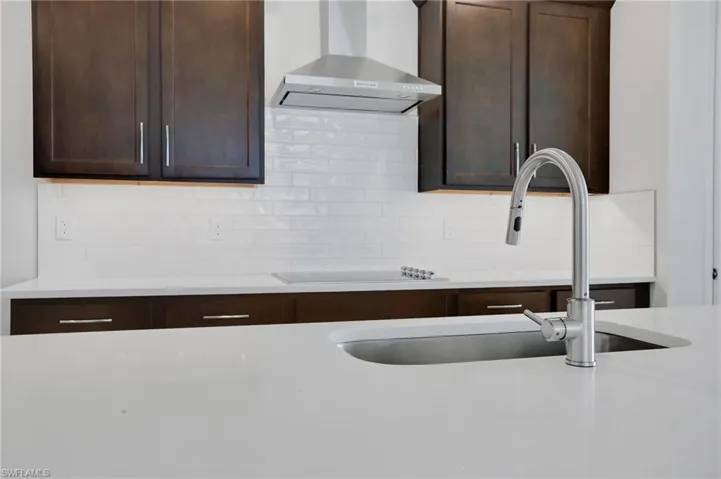 Kitchen featuring dark wood finish cabinetry, light stone countertops, tasteful backsplash, and black electric stovetop